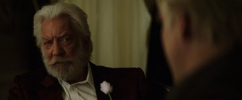Movie still from “The Hunger Games: Catching Fire” (2013), directed by Francis Lawrence – An older man sitting in front of a curtain; Close Up shot, Over the shoulder angle