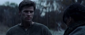 Movie still from “The Hunger Games: Catching Fire” (2013), directed by Francis Lawrence – A young man in a gray shirt is standing in the woods; Close Up shot, Over the shoulder angle