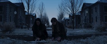 Movie still from “The Hunger Games: Catching Fire” (2013), directed by Francis Lawrence – Two young women kneeling on the ground in front of a row of houses; Wide shot, Low angle
