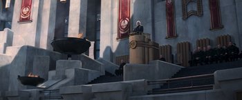 Movie still from “The Hunger Games: Catching Fire” (2013), directed by Francis Lawrence – A man standing at a podium speaking; Extreme Wide shot, High angle