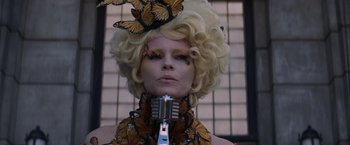 Movie still from “The Hunger Games: Catching Fire” (2013), directed by Francis Lawrence – A woman with blonde hair wearing a butterfly necklace; Close Up shot, Low angle