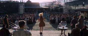 Movie still from “The Hunger Games: Catching Fire” (2013), directed by Francis Lawrence – A crowd of people are gathered in front of a stage; Wide shot, High angle