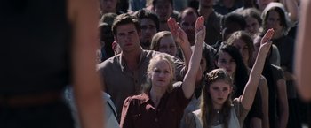 Movie still from “The Hunger Games: Catching Fire” (2013), directed by Francis Lawrence – A woman raises her hand in front of a crowd of onlookers; Medium shot, High angle