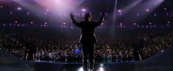 Movie still from “The Hunger Games: Catching Fire” (2013), directed by Francis Lawrence – A man standing in front of an audience on a stage; Wide shot, Low angle