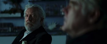 Movie still from “The Hunger Games: Catching Fire” (2013), directed by Francis Lawrence – A man with white hair and a white beard is sitting in front of another man with white hair; Close Up shot, Over the shoulder angle