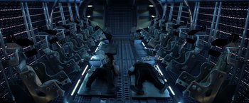 Movie still from “The Hunger Games: Catching Fire” (2013), directed by Francis Lawrence – Two men laying down in an airplane with rows of seats in front of them; Wide shot, Overhead angle