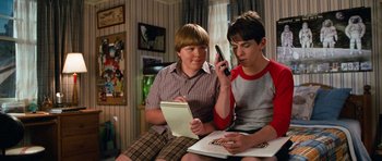 Movie still from “Diary of a Wimpy Kid: Dog Days” (2012), directed by David Bowers – Two young men are sitting in a living room; Medium shot, High angle