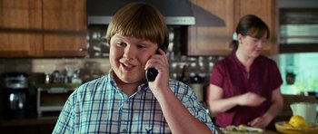 Movie still from “Diary of a Wimpy Kid: Dog Days” (2012), directed by David Bowers – A young boy talking on a cell phone in a kitchen; Medium shot, Over the shoulder angle