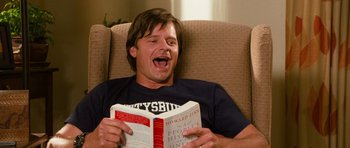 Movie still from “Diary of a Wimpy Kid: Dog Days” (2012), directed by David Bowers – A man sitting in a chair holding an open book; Medium shot, High angle