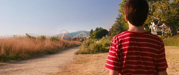 Movie still from “Diary of a Wimpy Kid: Dog Days” (2012), directed by David Bowers – A man standing on a dirt road near a park; Extreme Wide shot, Over the shoulder angle