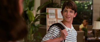 Movie still from “Diary of a Wimpy Kid: Dog Days” (2012), directed by David Bowers – A young man holding a backpack and smiling for the camera; Close Up shot, High angle