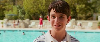 Movie still from “Diary of a Wimpy Kid: Dog Days” (2012), directed by David Bowers – A young man smiles at the camera in front of a swimming pool; Close Up shot, High angle