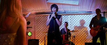 Movie still from “Diary of a Wimpy Kid: Dog Days” (2012), directed by David Bowers – A woman holding a microphone while standing in front of a band; Medium shot, Over the shoulder angle