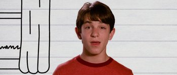 Movie still from “Diary of a Wimpy Kid: Dog Days” (2012), directed by David Bowers – A young man in a red t - shirt is standing in front of a white wall; Close Up shot, Low angle