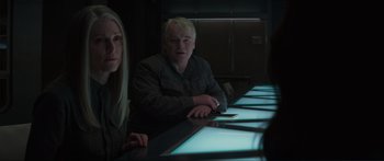 Movie still from “The Hunger Games: Mockingjay - Part 1” (2014), directed by Francis Lawrence – A man and a woman sitting at a table in a dark room; Medium shot, Over the shoulder angle