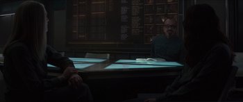 Movie still from “The Hunger Games: Mockingjay - Part 1” (2014), directed by Francis Lawrence – A group of people sitting at a table in a dark room; Medium shot, Over the shoulder angle