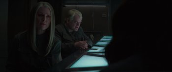 Movie still from “The Hunger Games: Mockingjay - Part 1” (2014), directed by Francis Lawrence – A man sitting at a table with a pen in his hand; Medium shot, Over the shoulder angle
