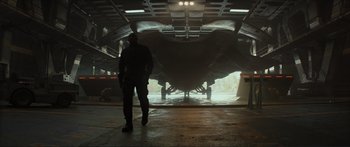 Movie still from “The Hunger Games: Mockingjay - Part 1” (2014), directed by Francis Lawrence – A man standing in front of an airplane in a hangar; Wide shot, Low angle