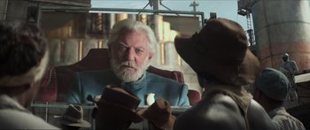 Movie still from “The Hunger Games: Mockingjay - Part 1” (2014), directed by Francis Lawrence – An older man looking in the mirror while wearing a hat; Medium shot, Over the shoulder angle