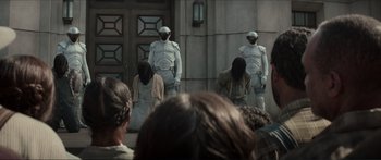 Movie still from “The Hunger Games: Mockingjay - Part 1” (2014), directed by Francis Lawrence – A group of people standing in front of a building; Medium shot, Over the shoulder angle