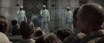 Movie still from “The Hunger Games: Mockingjay - Part 1” (2014), directed by Francis Lawrence – A group of men in white costumes performing on a stage; Wide shot, Over the shoulder angle