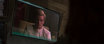 Movie still from “The Hunger Games: Mockingjay - Part 1” (2014), directed by Francis Lawrence – A man in a white suit sitting in front of a television; Close Up shot, Over the shoulder angle