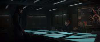 Movie still from “The Hunger Games: Mockingjay - Part 1” (2014), directed by Francis Lawrence – A man sitting in front of a large table with lights on it; Wide shot, High angle