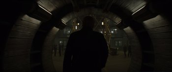 Movie still from “The Hunger Games: Mockingjay - Part 1” (2014), directed by Francis Lawrence – A man standing in a dark tunnel with people in the background; Wide shot, Over the shoulder angle