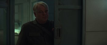 Movie still from “The Hunger Games: Mockingjay - Part 1” (2014), directed by Francis Lawrence – A man standing next to a door in a dark room; Close Up shot, Over the shoulder angle