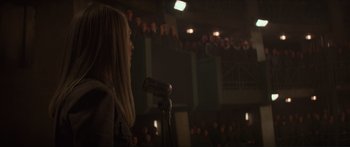 Movie still from “The Hunger Games: Mockingjay - Part 1” (2014), directed by Francis Lawrence – A woman standing at a microphone in front of an audience; Medium shot, Over the shoulder angle