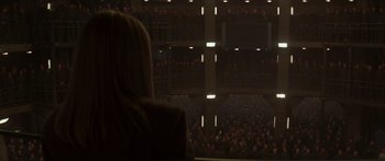 Movie still from “The Hunger Games: Mockingjay - Part 1” (2014), directed by Francis Lawrence – A woman sitting in front of an audience in a theater; Extreme Wide shot, High angle