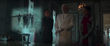 Movie still from “The Hunger Games: Mockingjay - Part 1” (2014), directed by Francis Lawrence – A man in a white suit standing next to another man in a military uniform; Wide shot, Low angle