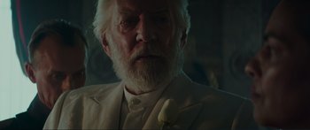 Movie still from “The Hunger Games: Mockingjay - Part 1” (2014), directed by Francis Lawrence – An old man with a white beard and a white flower in his lapel; Close Up shot, Over the shoulder angle