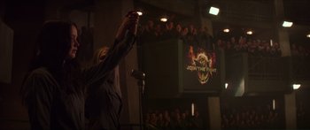 Movie still from “The Hunger Games: Mockingjay - Part 1” (2014), directed by Francis Lawrence – A person holding a microphone in front of an audience; Wide shot, Low angle