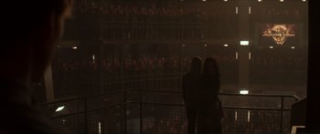 Movie still from “The Hunger Games: Mockingjay - Part 1” (2014), directed by Francis Lawrence – Two women standing in front of an audience in front of a fence; Extreme Wide shot, High angle