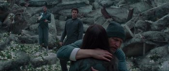 Movie still from “The Hunger Games: Mockingjay - Part 1” (2014), directed by Francis Lawrence – Two men and a woman hugging in a rocky area; Medium shot, Over the shoulder angle