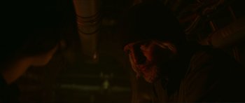 Movie still from “The Hunger Games: Mockingjay - Part 1” (2014), directed by Francis Lawrence – A man with long hair and a goatee is in the dark; Close Up shot, Over the shoulder angle