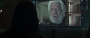 Movie still from “The Hunger Games: Mockingjay - Part 1” (2014), directed by Francis Lawrence – An old man with white hair is on a television screen; Close Up shot, Over the shoulder angle
