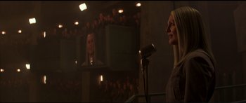 Movie still from “The Hunger Games: Mockingjay - Part 1” (2014), directed by Francis Lawrence – A woman standing in front of a microphone in front of an audience; Medium shot, Low angle