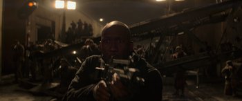 Movie still from “The Hunger Games: Mockingjay - Part 2” (2015), directed by Francis Lawrence – A man holding a gun in front of an audience; Close Up shot, Low angle