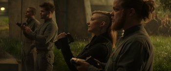 Movie still from “The Hunger Games: Mockingjay - Part 2” (2015), directed by Francis Lawrence – A woman sitting in a field with two men; Medium shot, Low angle