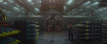 Movie still from “The Hunger Games: Mockingjay - Part 2” (2015), directed by Francis Lawrence – Two men standing in a large room with a large machine in the middle of the room; Extreme Wide shot, High angle