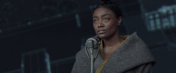 Movie still from “The Hunger Games: Mockingjay - Part 2” (2015), directed by Francis Lawrence – A woman standing in front of a microphone in a dark room; Close Up shot, Over the shoulder angle