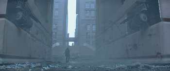Movie still from “The Hunger Games: Mockingjay - Part 2” (2015), directed by Francis Lawrence – A person standing in a room with a building in the background; Extreme Wide shot, Low angle