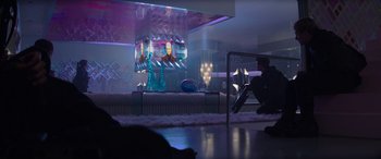 Movie still from “The Hunger Games: Mockingjay - Part 2” (2015), directed by Francis Lawrence – A man sitting on the ground in front of a television; Wide shot, Over the shoulder angle