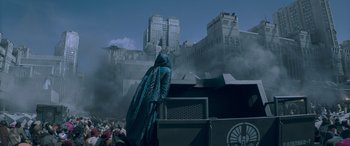 Movie still from “The Hunger Games: Mockingjay - Part 2” (2015), directed by Francis Lawrence – A man in a hooded cloak standing in front of a building; Wide shot, Low angle