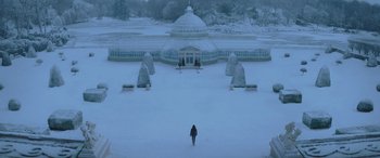 Movie still from “The Hunger Games: Mockingjay - Part 2” (2015), directed by Francis Lawrence – A person is walking in the snow near a greenhouse; Extreme Wide shot, High angle