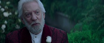 Movie still from “The Hunger Games: Mockingjay - Part 2” (2015), directed by Francis Lawrence – An older man with a white rose in his lapel; Close Up shot, Over the shoulder angle