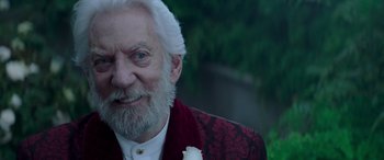 Movie still from “The Hunger Games: Mockingjay - Part 2” (2015), directed by Francis Lawrence – An older man with a white beard and a white rose in his mouth; Close Up shot, Over the shoulder angle