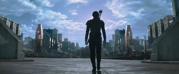 Movie still from “The Hunger Games: Mockingjay - Part 2” (2015), directed by Francis Lawrence – A man holding a bow and arrow in the middle of a city; Wide shot, Low angle